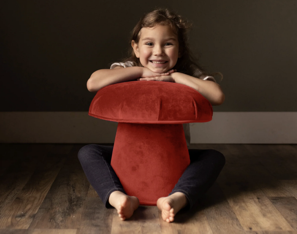 A girl resting her head on a Velvet Mushroom Stool in Coral